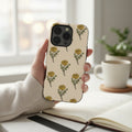 La Apau Creations phone case with hand-drawn yellow marigold floral pattern on a cream background held in a hand